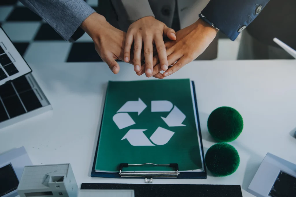 Três mãos de empresários unidas simbolizando colaboração, com um símbolo de logística reversa abaixo representando sustentabilidade e retorno de produtos.