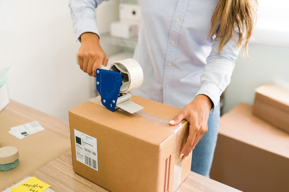 Mulher embalando produto utilizando o packing para otimizar os custos operacionais em logística.